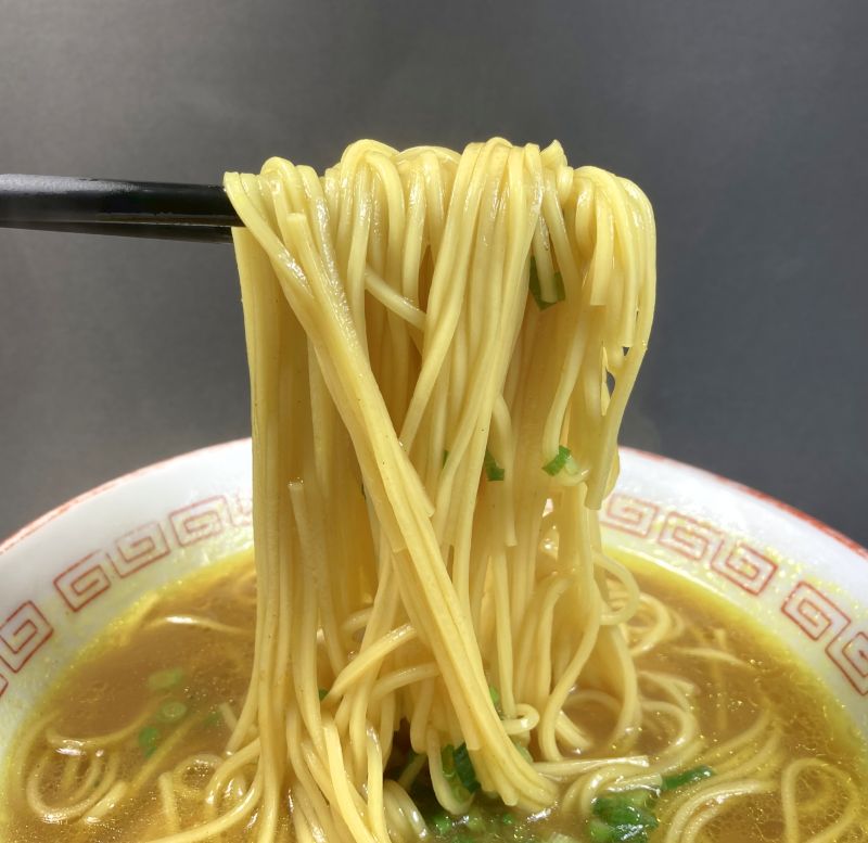 日の出製粉株式会社 カレーラーメン スパイシーカレー味 カレー龍の麺をはしでつまむ