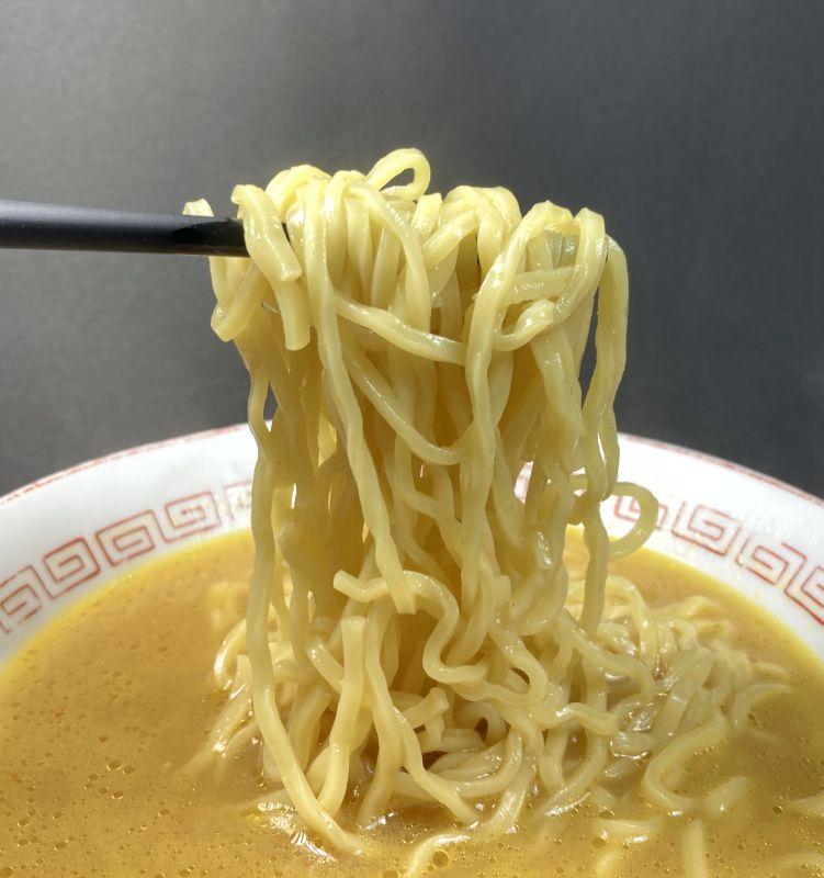 高砂食品株式会社 青森発 味噌カレー牛乳らぁめんの麺を箸でつまむ